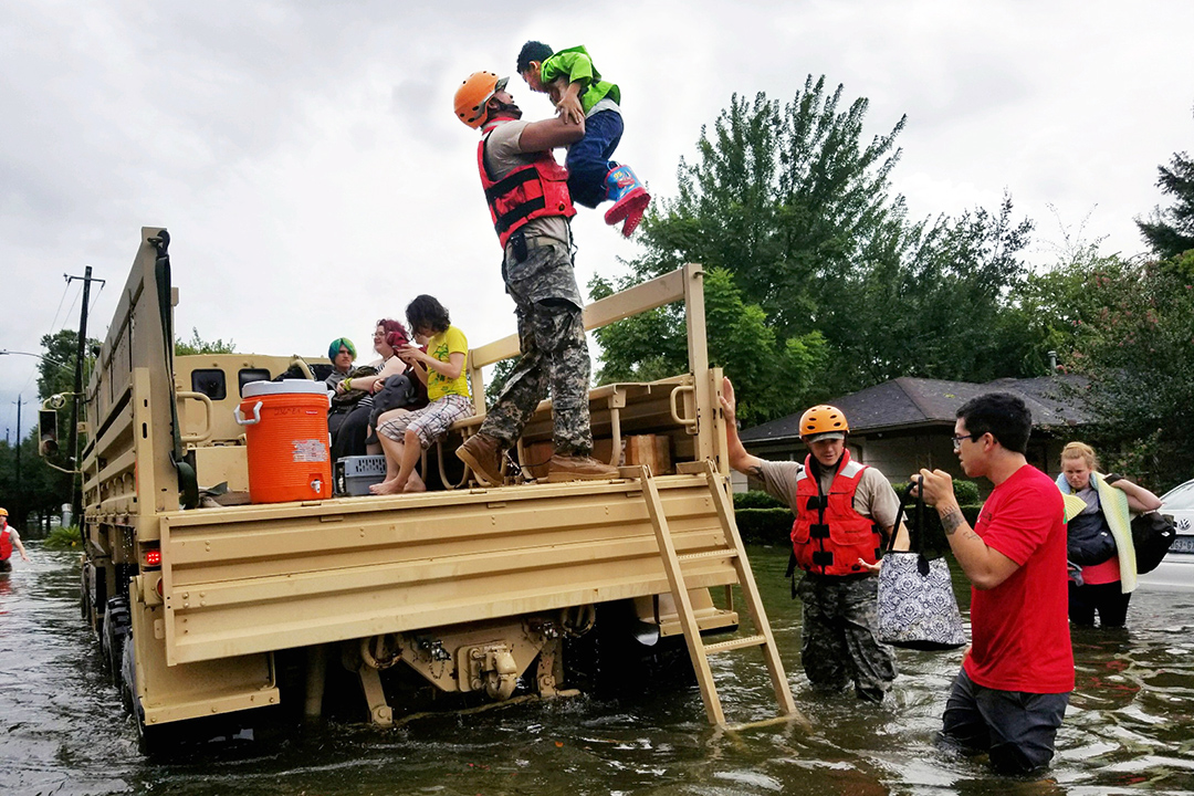 Survivors wade through floodwater while a rescuer lifts a young boy onto a truck