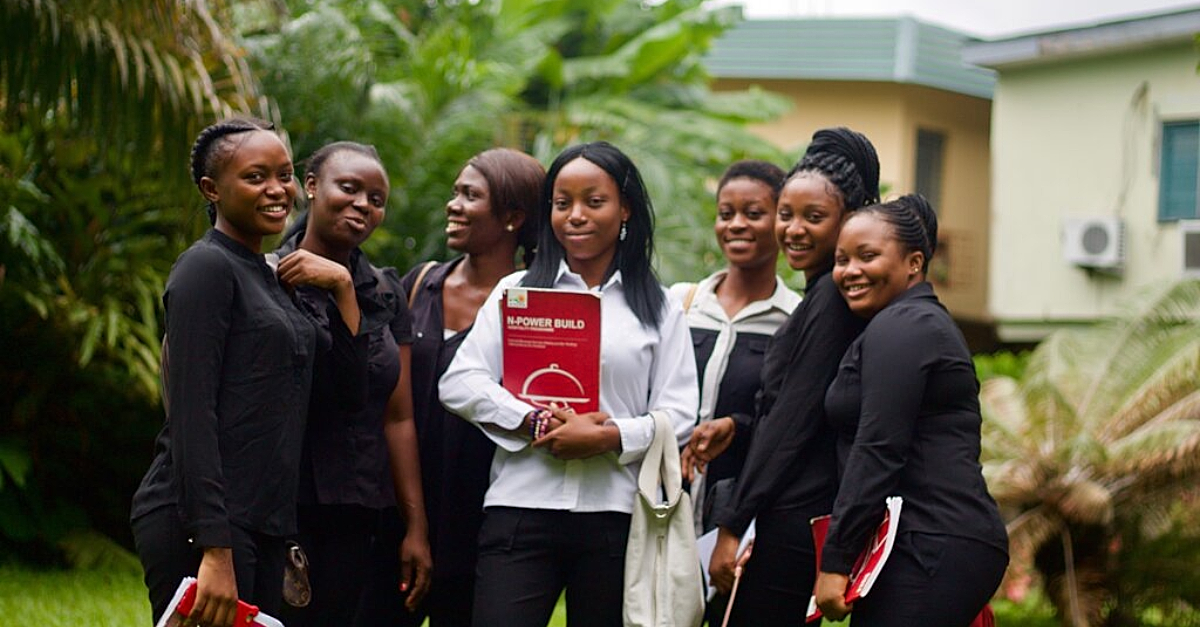 Group of girls smile at the camera, some hold textbooks. corporate employee experience